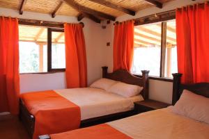 拉基拉Posada El Artesano De Raquira的一间卧室设有两张床,窗户配有橙色窗帘
