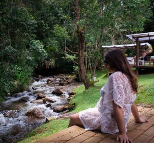 圣弗朗西斯科泽维尔Pousada Vila Santa Barbara的坐在溪流旁木桥上的女人