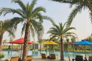 雅加达Studio Apartment - Gold Coast PIK, Jakarta Utara的一座棕榈树、椅子和遮阳伞的游泳池