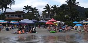 乌巴图巴Ubatuba Lagoinha Salga Mini Resort的一群人坐在海滩上,拿着遮阳伞