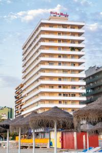 福恩吉罗拉Apartamentos Stella Maris - Marcari SL的海滩上一座带稻草遮阳伞的高楼