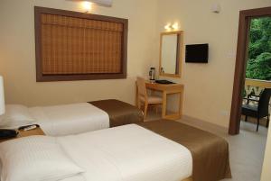 帕纳吉Sandalwood Hotel & Suites的酒店客房设有两张床、一张桌子和一面镜子