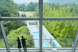 松山SETOUCHI RETREAT by Onko Chishin的两个人站在一座建筑物里,看着一个游泳池