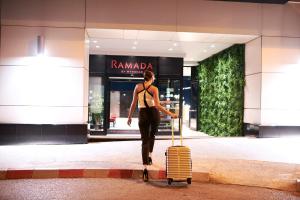 波德戈里察Ramada by Wyndham Podgorica的带着手提箱在商店前走的女人