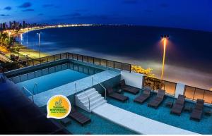若昂佩索阿卡博布兰科阿特兰蒂克酒店的一个带椅子的游泳池,晚上则在海滩上