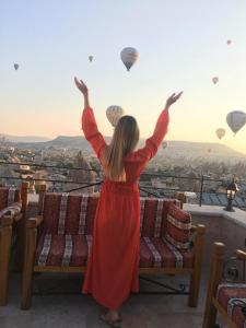 格雷梅Cappadocia Cave Lodge的穿着红色衣服的女人看着热气球
