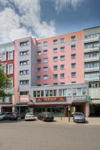 柏林City Hotel Ansbach am KaDeWe的一座大型粉红色建筑,前面有汽车停放