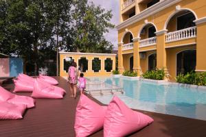 甲米镇The Pineapple Hotel的一名妇女和一名儿童在游泳池边散步,游泳池边配有粉红色枕头