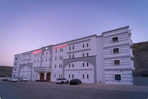 马斯喀特利雅姆酒店的一座白色的大建筑,汽车停在停车场
