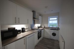 德里门Loch Lomond Riverside Apartment的厨房配有白色橱柜、洗衣机和烘干机