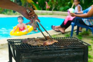 米卡Domo 1 en la selva a 3 km de Minca的游泳池旁的烤架上有人烹饪肉