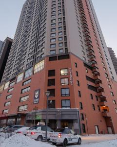 阿斯塔纳Elite apartments的一座高大的建筑,前面有汽车停放