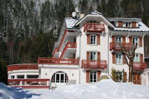 夏蒙尼-勃朗峰Chalet Hôtel La Sapinière的白色的大房子,在雪中设有红色的阳台