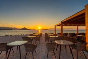 派尔季卡LaLiBay Resort & Spa - Adults Only的日落时在海滩上摆放着几张桌子和椅子