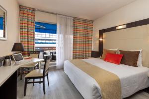 圣罗兰度瓦The Originals City, Hôtel Galaxie, Nice Aéroport的配有一张床、一张桌子和一张桌子的酒店客房