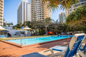 黄金海岸海滨庄园度假酒店的一座带椅子和棕榈树的游泳池以及建筑
