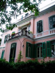 的里雅斯特法伍斯塔别墅住宿加早餐旅馆的粉红色的房子,设有绿色百叶窗和阳台