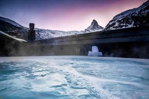 采尔马特Hotel ZERMAMA Zermatt的热水浴池后面有积雪覆盖的群山