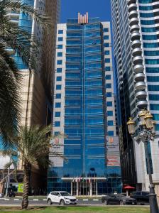 沙迦沙迦国敦大酒店的一座高大的蓝色建筑,前面有汽车停放