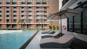 北芭堤雅Mandarin Eastville, Pattaya - SHA Extra Plus的一座带椅子和遮阳伞的游泳池位于大楼旁