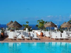 阿德耶火烈鸟海滩伴侣公寓的度假村的游泳池配有白色椅子和遮阳伞