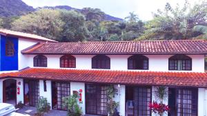 特林达德Pousada Em Busca do Sol的白色的房子,有红色的屋顶和树木