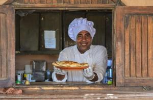 ‘Ezbet HalfaQasr El Bagawat Hotel的厨师在厨房里拿着一盘比萨饼