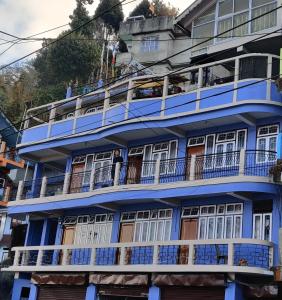 大吉岭West Point Backpackers Hostel的蓝色的建筑,设有白色的窗户和阳台