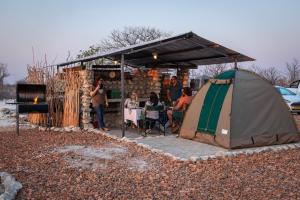 奥考奎约Etosha Trading Post Campsite的一群人坐在帐篷下的桌子上