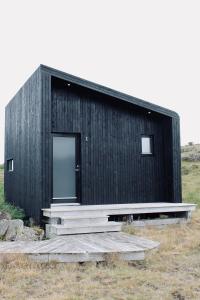 Sandgerði爱思戴小屋酒店的一座黑色的建筑,在田野上有一扇门