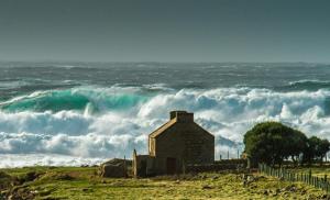 Tory IslandOstán Oileán Thoraí Tory Island Hotel的海滩上一座老建筑,波浪很大