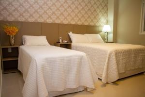 Telêmaco BorbaHotel Seville Comfort的配有白色床单的酒店客房内的两张床