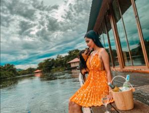 北碧Kodaun River Kwai Resort的站在水体旁边的一个身着橙色衣服的女人