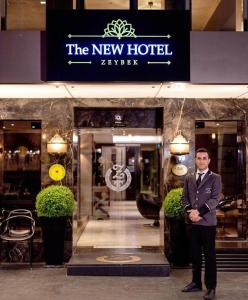伊兹密尔The New Hotel Zeybek的站在酒店前身的身着西装的男人