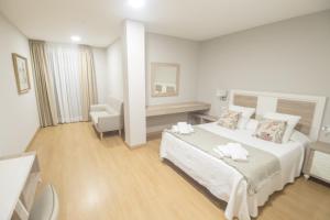 卡尔达斯·德·雷斯Hotel Roquiño的白色卧室配有一张大床和椅子