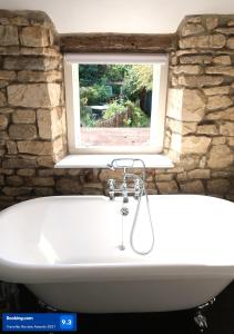 温什科姆Boutique cottage in the heart of Winchcombe的浴缸位于带窗户的石墙前