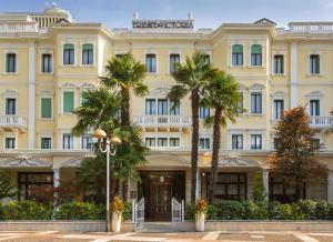 阿巴诺泰尔梅特里雅斯特和维多利亚大酒店的一座黄色的大建筑,前面有棕榈树