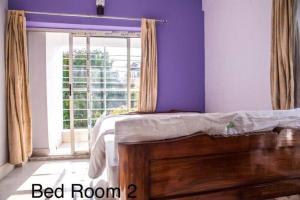 加尔各答Diamond By Olys Apartment的一间卧室配有一张紫色墙壁和窗户的床