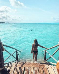 江比阿Reef & Beach Resort - Spa Jambiani的一位在码头上走入水中的女人