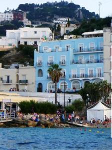 卡普里Relais Maresca Luxury Small Hotel & Terrace Restaurant的一座蓝色的建筑,人们在海滩上,在水面前