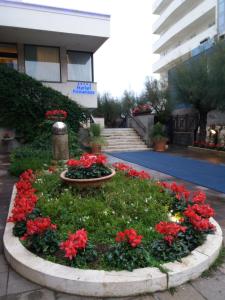 蒙特西尔瓦诺海滨长廊酒店的一座圆形花园,在一座建筑前方种有红色花卉