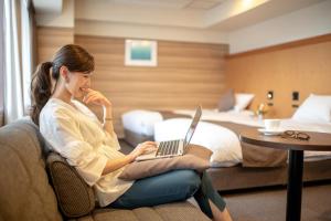 新泻新泻大酒店 的坐在酒店房间一张带笔记本电脑的沙发上的女人