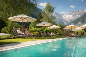 布兰德微拉阿凯提度假酒店的两人坐在泳池旁的椅子上,旁边摆放着遮阳伞