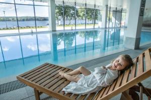 哈日科维Notera Hotel SPA的一个小女孩躺在游泳池旁边的长凳上