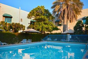 沙迦Al CORNICHE HOTEL的一座带椅子和遮阳伞的游泳池位于一座建筑旁边