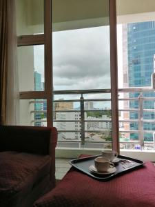 古晋StayInn Gateway Hotel Apartment的窗前桌子上装有两个咖啡杯的托盘