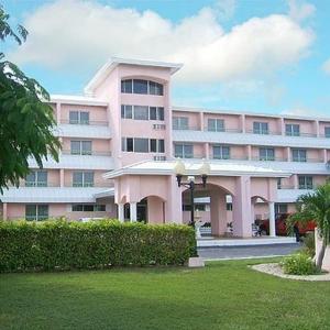 自由港市卡斯塔韦斯套房度假村酒店的一座大型粉红色建筑,前面有一棵棕榈树