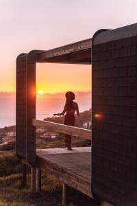 卡列塔Calheta Glamping Pods - Nature Retreat的站在长凳上看着日落的女人