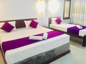 阿努拉德普勒Cumini Resort的宿舍间内的两张床,配有红色和紫色枕头