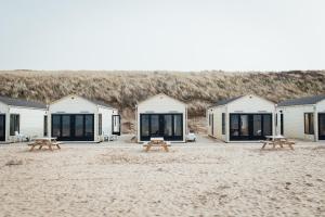 滨海卡特韦克Logeren aan Zee的海滩上一排带野餐桌的小屋